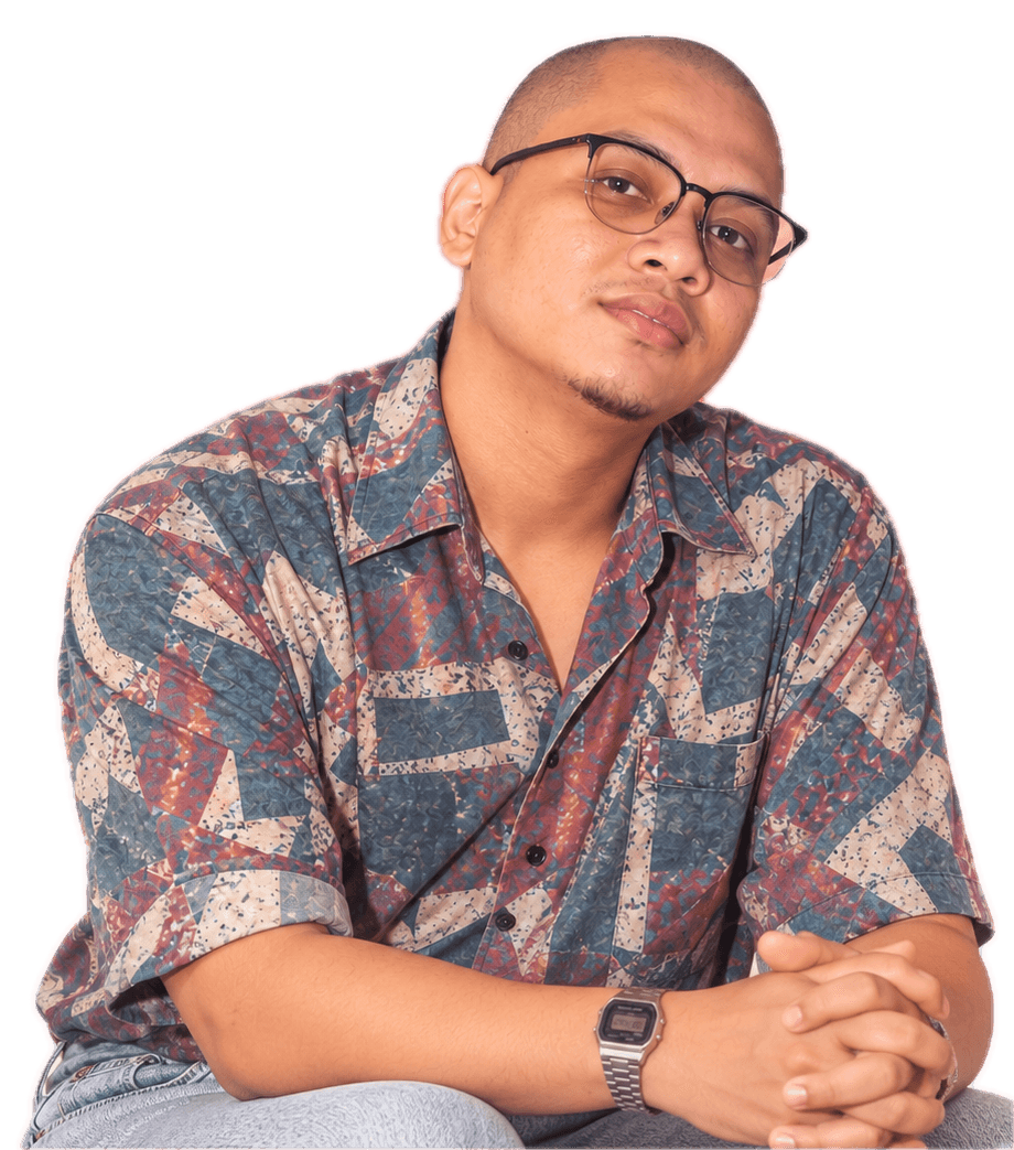 Portrait of Farid Aiman in a patterned shirt, leaning forward with hands clasped